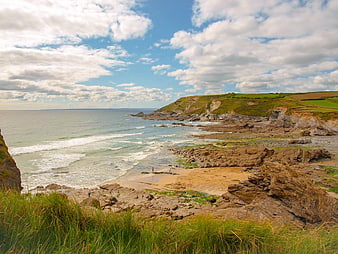 Scenic coastal landscape with rocky cliffs, sandy beach, and blue sky