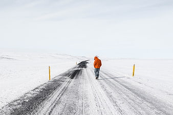 Man in Orange Jacket Walking on Snowy Winter Road