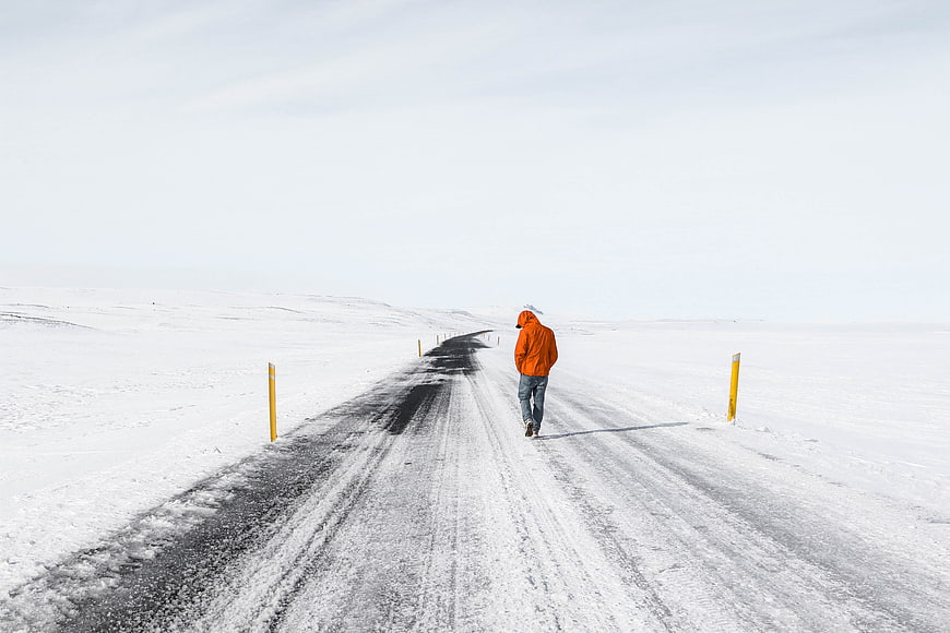 Man in Orange Jacket Walking on Snowy Winter Road