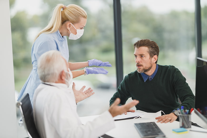 Upset male patient arguing with doctor and nurse in clinic