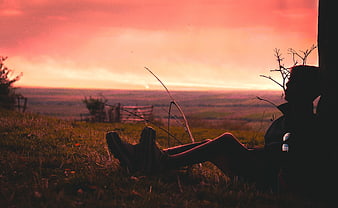 Silhouette of Man Relaxing on Hillside at Sunset
