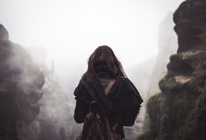 Woman with backpack looking at misty rock formations
