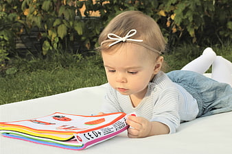 Toddler girl reading colorful book on white blanket outdoors