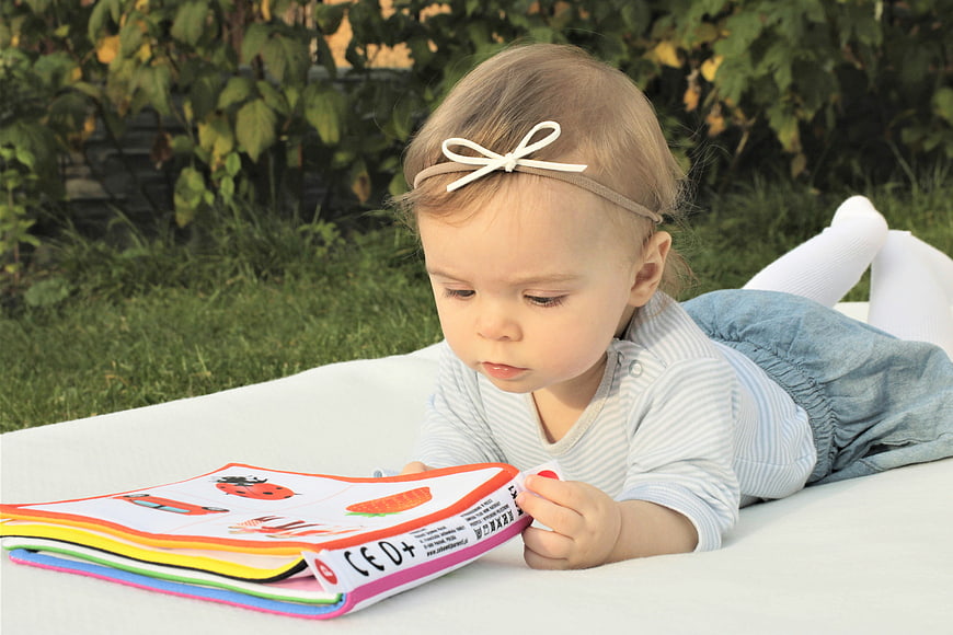 Toddler girl reading colorful book on white blanket outdoors