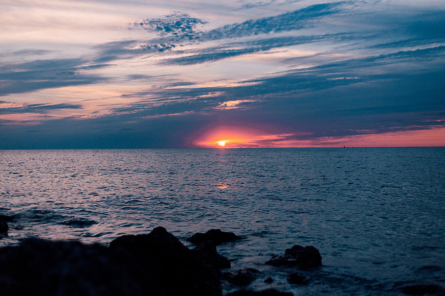 Serene Sunset Over Ocean with Silhouetted Rocks and Colorful Sky