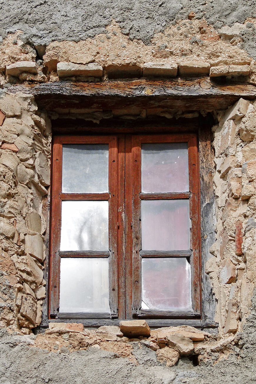 Old wooden window in weathered stone wall