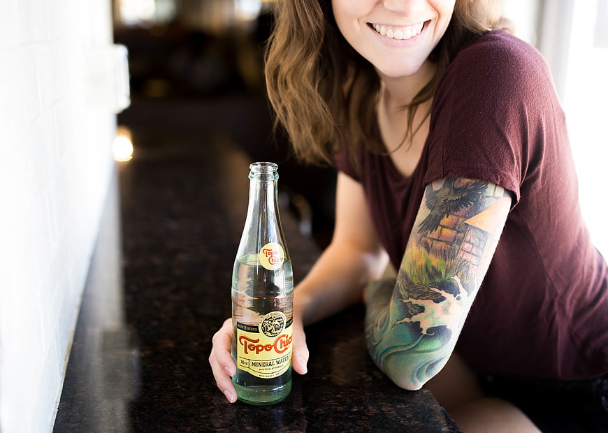 Smiling Woman with Tattoo Holding Topo Chico Bottle