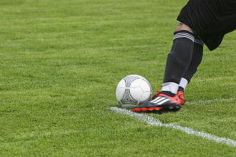 Soccer player foot on ball at white line on green grass field