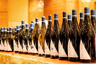 Rows of wine bottles on a wooden shelf with warm lighting