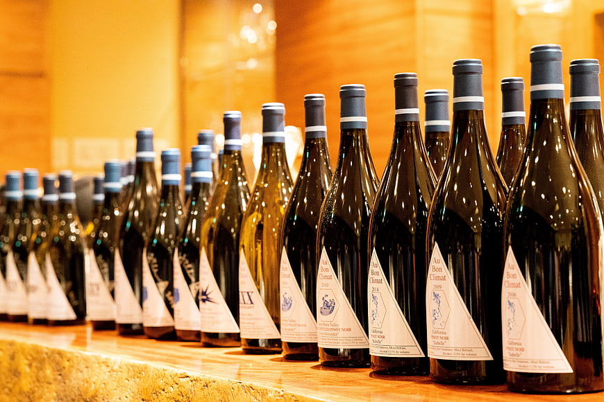 Rows of wine bottles on a wooden shelf with warm lighting