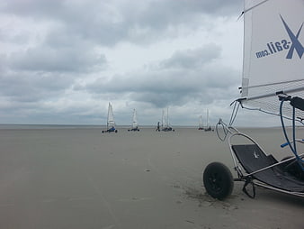 Land sailing buggies on a wide sandy beach under cloudy sky