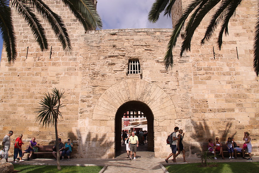 Tourists walking through historic stone fortress gate with palm trees