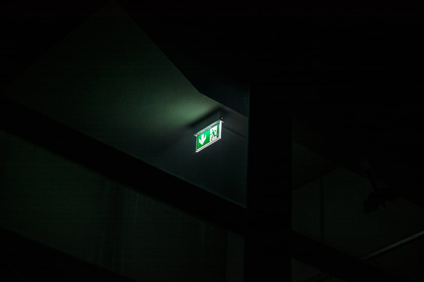 Illuminated green emergency exit sign in dark industrial interior