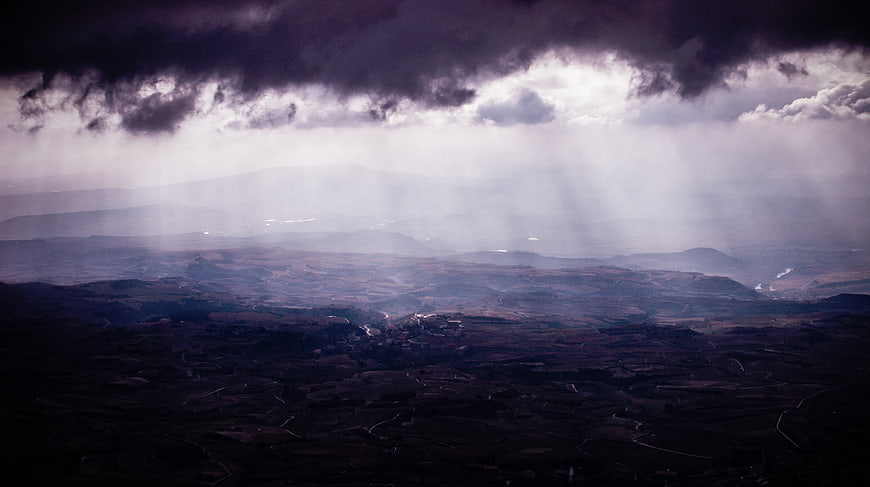 Dramatic Storm Clouds Over Rolling Hills with Sunbeams