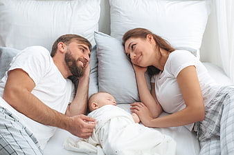 Happy Parents Watching Sleeping Newborn Baby in Bed