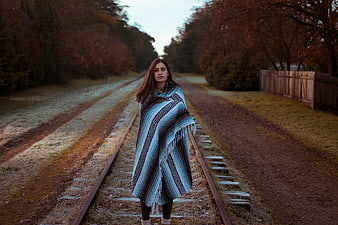 Woman in Patterned Poncho Standing on Railway Tracks
