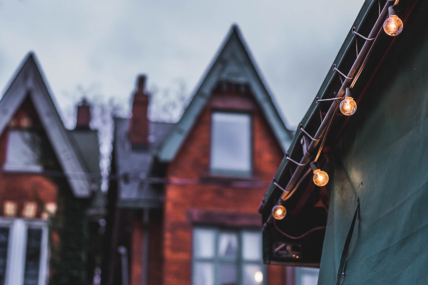 String lights on green roof with blurred brick houses