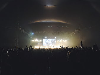 Concert crowd silhouettes with raised hands facing a brightly lit stage