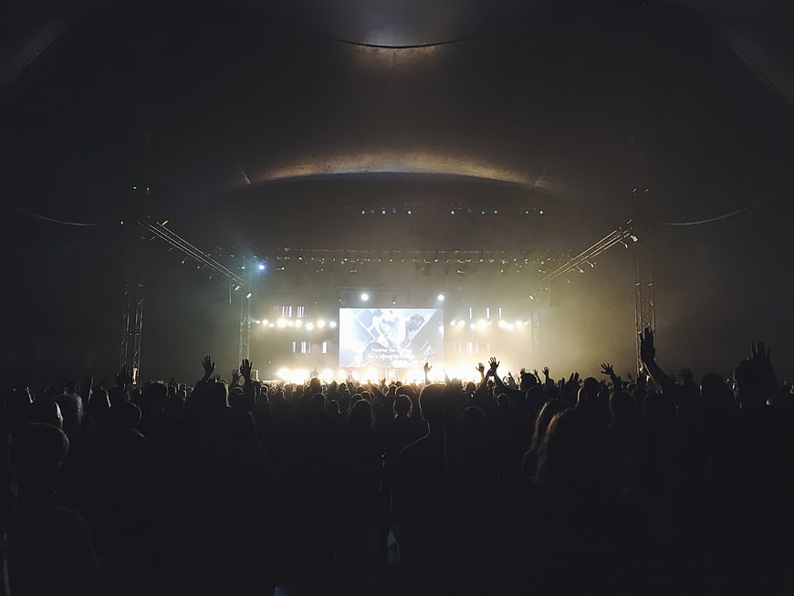 Concert crowd silhouettes with raised hands facing a brightly lit stage