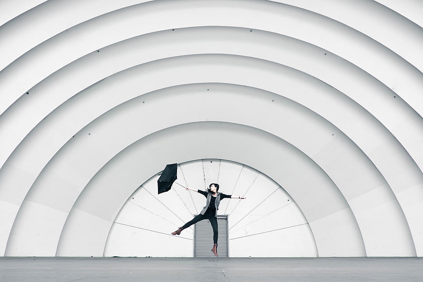 Woman Leaping With Umbrella Under White Architectural Arches