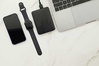 Flat lay of laptop, smartphone, smartwatch, and external hard drive on marble