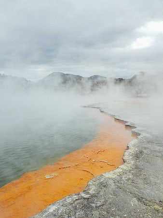 Steaming orange thermal pool with misty mountain backdrop
