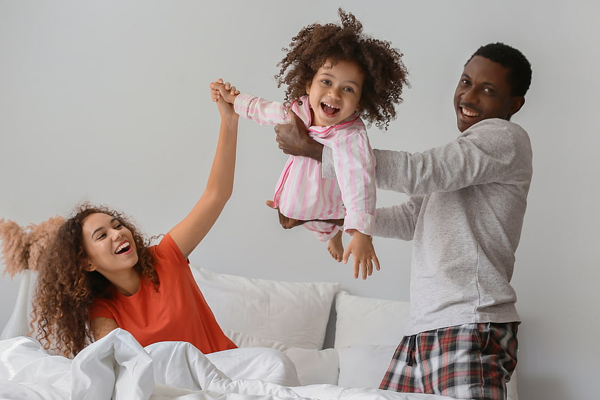 Happy African American Family Playing in Bed with Toddler