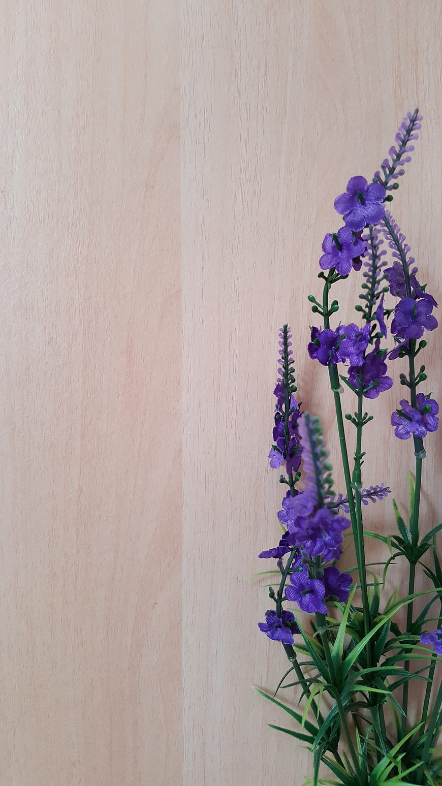 Purple artificial flowers on light wood background with copyspace