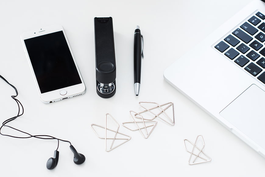 Minimalist white desk with laptop, smartphone, and office supplies