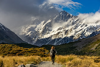 Female Hiker Walking on Mountain Trail with Snowy Peaks