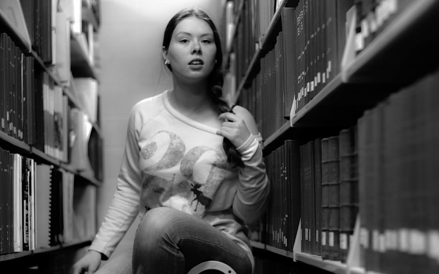 Young woman sitting in library aisle holding braid