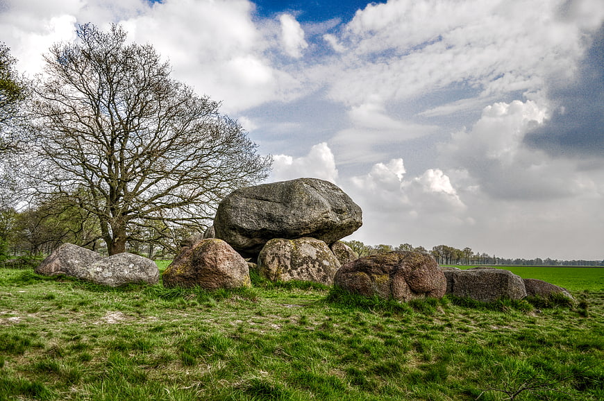 Ancient megalithic tomb in green field under cloudy sky