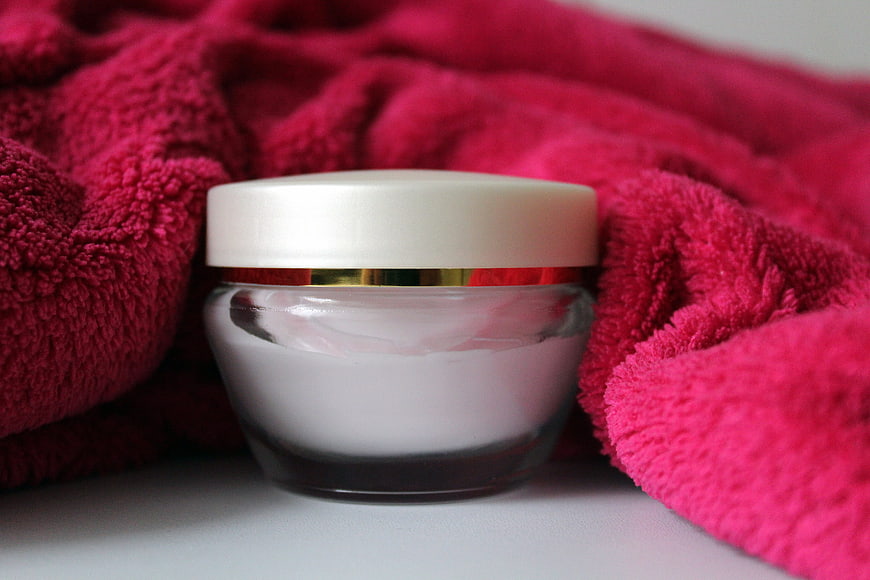 Luxury white cosmetic cream jar with gold rim on pink towel
