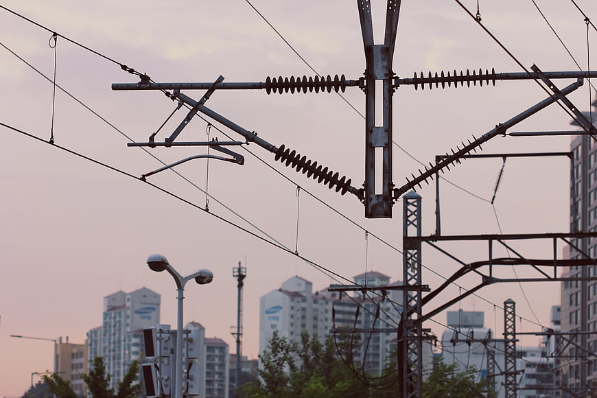 Overhead Railway Catenary System Against Urban Skyline At Dusk