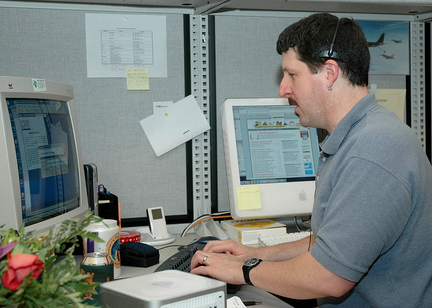 Man working at dual computer monitors in office cubicle