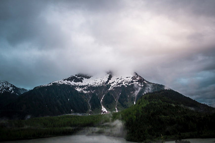 Dramatic Snow-Capped Mountain Peak with Clouds and Forest