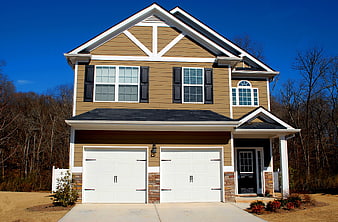 Two-Story Tan House With White Garage Doors And Blue Sky