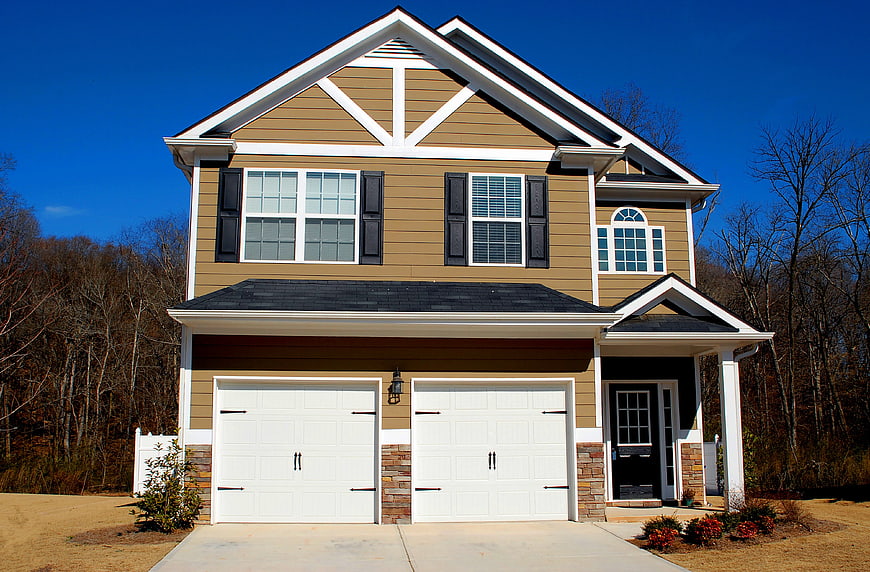 Two-Story Tan House With White Garage Doors And Blue Sky