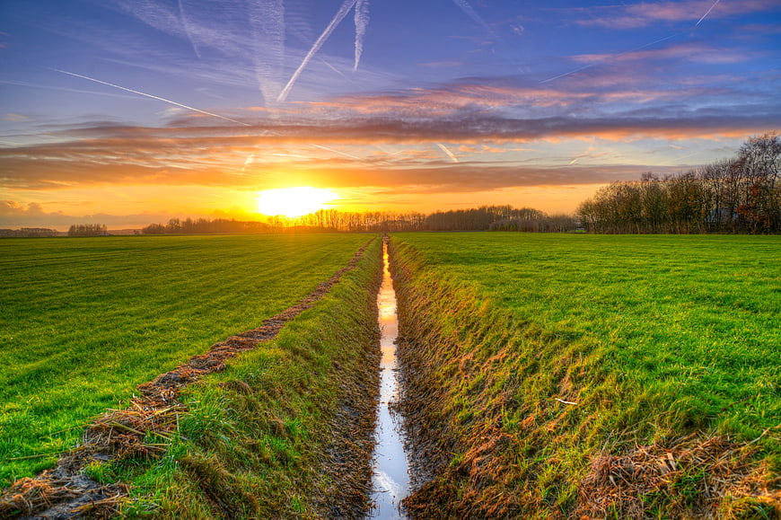 Sunset over Green Meadow with Ditch and Contrails