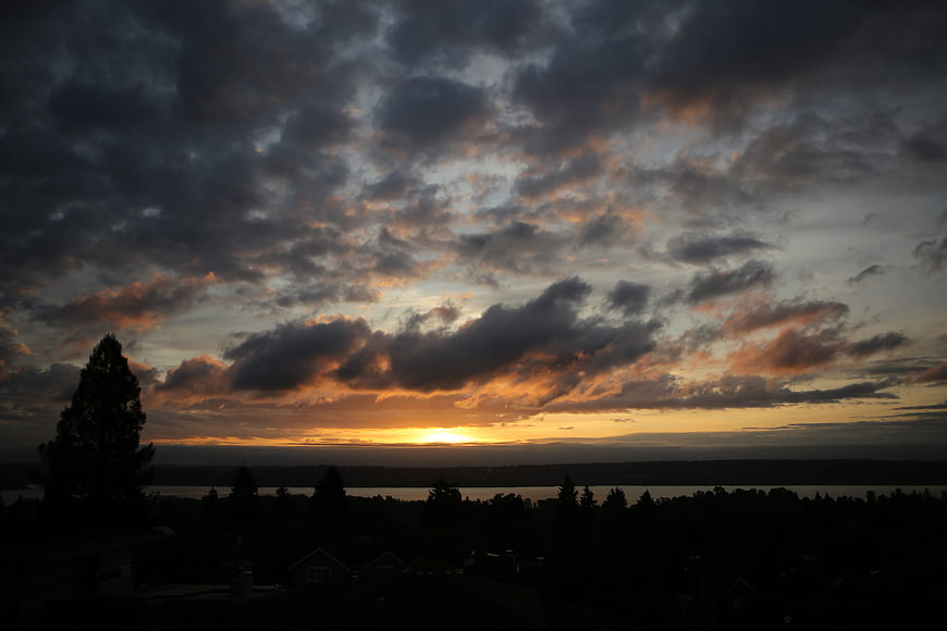 Dramatic sunset over lake with silhouetted trees and clouds