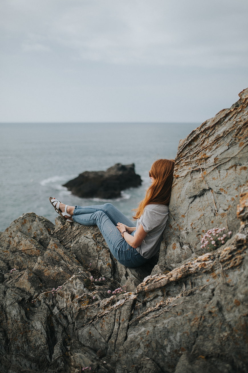 Redhead woman sitting on rocky cliff overlooking ocean
