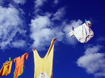 Colorful baby clothes hanging on a clothesline against a bright blue sky