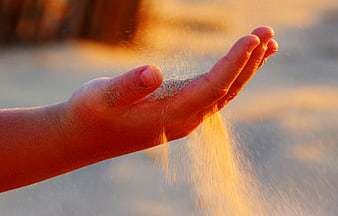 Sand trickling through open hand in warm golden hour light