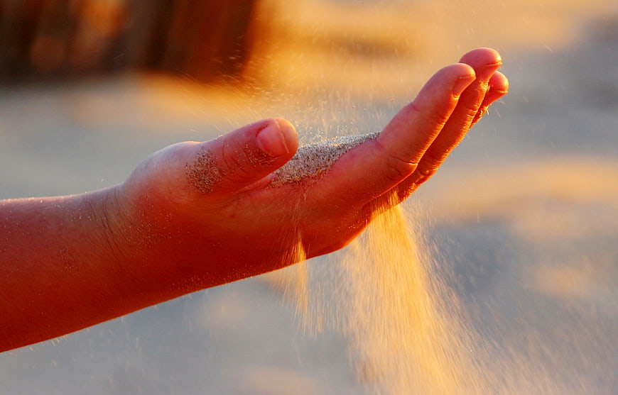 Sand trickling through open hand in warm golden hour light