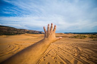 Hand Reaching Out Over Sand Dunes in Desert Landscape