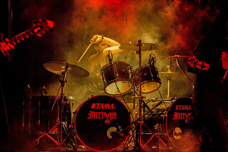 Energetic Drummer Performing on Stage with Red Lighting