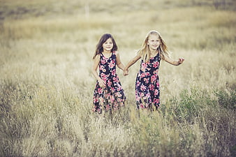 Two young girls running hand in hand through a grassy field