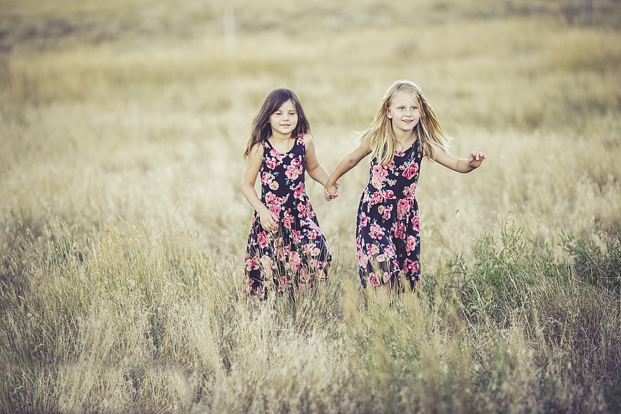 Two young girls running hand in hand through a grassy field
