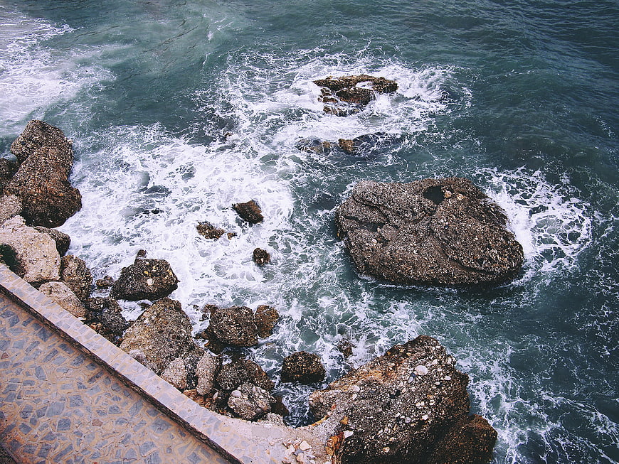 Aerial View of Turbulent Ocean Waves Crashing Against Rocky Coastline