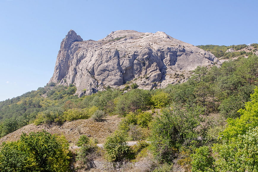 Rugged limestone mountain peak with green forest and blue sky